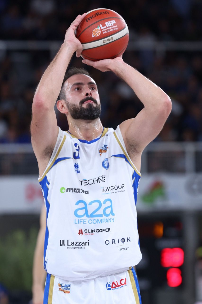Giocatore Leonessa Basket Brescia in azione, concentrato durante un tiro libero, indossa una maglia bianca sponsorizzata.